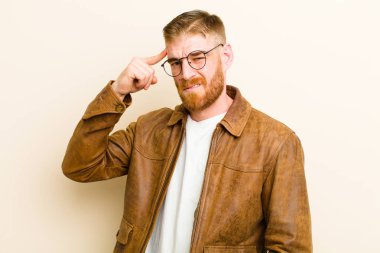 Genç kızıl saçlı adam şaşkın ve şaşkın hissediyor, deli olduğunu gösteriyor, ya da bej arka plana karşı aklını kaçırdığını.