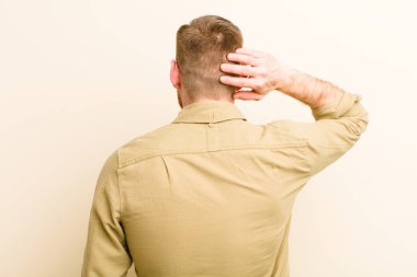 Genç kızıl saçlı adam düşünüyor ya da şüphe ediyor, kaşınıyor, kafası karışık ve şaşkın hissediyor, bej arka plan ya da arka plan