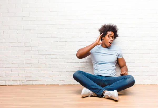 若い黒人男性は笑顔で横を見 ゴシップを聴こうとしたり 家の床に座って秘密を聞こうとしています — ストック写真