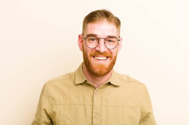 Genç kızıl saçlı, büyük, dost canlısı, kaygısız gülüşlü, pozitif, rahat ve mutlu görünen, bej arka planda takılan