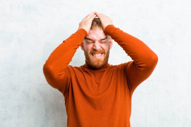 Kaplumbağa boynu takan genç kızıl adam stresli ve endişeli, bunalımda ve hayal kırıklığına uğramış, iki elini de beton duvara doğru kaldırıyor.