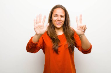 Genç bayan gülümsüyor ve arkadaş canlısı görünüyor, 8 ya da 8 numarayı gösteriyor, beyaz arka planda geriye doğru sayıyor.