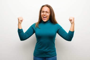 Genç bir kadın mutlu, şaşırmış ve gururlu, beyaz arka planda büyük bir gülümsemeyle bağırıyor ve başarıyı kutluyor.