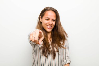 Genç bir kadın kameraya tatmin olmuş, kendinden emin, arkadaş canlısı bir gülümsemeyle bakıyor, beyaz arka planda seni seçiyor.