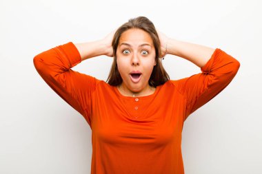 Genç bir kadın heyecanlı ve şaşırmış görünüyor, ağzı açık, elleri başının üstünde, beyaz arka plana karşı şanslı bir kazanan gibi hissediyor.