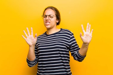 Genç, güzel bir kadın kışkırtıcı, agresif ve müstehcen hissediyor. Orta parmağını oynatıyor. Turuncu arka plana karşı isyankar bir tutum sergiliyor.