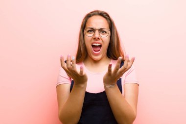 Genç kadın umutsuz ve hayal kırıklığına uğramış, stresli, mutsuz ve sinirli görünüyor, pembe arka planda bağırıyor ve çığlık atıyor.