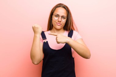 Sabırsız ve kızgın görünen genç bir kadın, saati göstererek, dakiklik sorarak, pembe arka plana karşı zamanında gelmek istiyor.