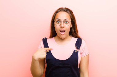 Şok olmuş ve şaşırmış görünen genç bir kadın ağzı açık, pembe arka planda kendini işaret ediyor.
