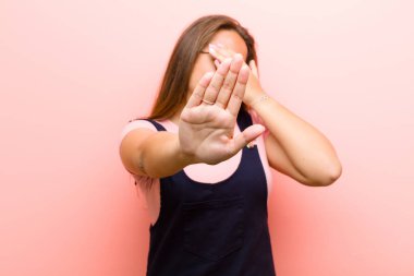 Genç bir kadın elini yüzünü örtüyor ve kamerayı durdurmak için diğer elini öne koyuyor. Pembe arka plandaki fotoğraf ve resimleri reddediyor.