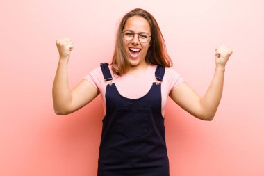 Genç bir kadın mutlu, şaşkın ve gururlu, pembe arka planda büyük bir gülümsemeyle bağırıyor ve başarıyı kutluyor.