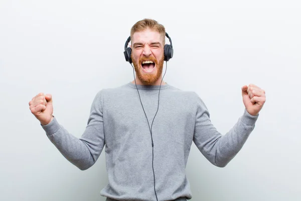 白い背景にヘッドフォンで音楽を聴いている若い赤い頭の男 — ストック写真