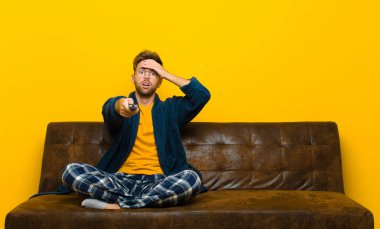 Genç adam pijama giyiyor ve uzaktan kumandalı bir kanepeye oturuyor.