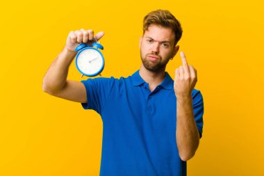 Turuncu arka planda çalar saati olan genç bir adam.