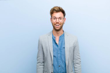 Genç işadamı mutlu ve hoş bir şekilde şaşırmış görünüyor, mavi arka plana karşı büyüleyici ve şok edici bir ifadeyle heyecanlanıyor.