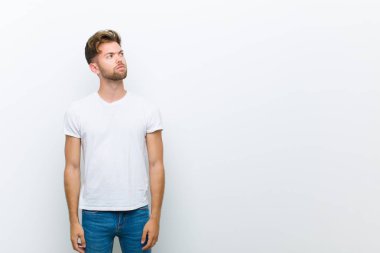 Endişeli, kafası karışık, budala bir ifadeyle genç bir adam, kopyalama alanına bakıyor, beyaz arka plana şüpheyle bakıyor.