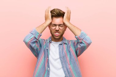 Genç adam stresli ve endişeli, depresif ve hayal kırıklığına uğramış, baş ağrısı ile, pembe arka plana karşı iki elini kaldırıyor