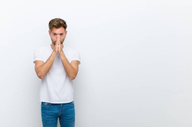 Genç adam endişeli, umutlu ve dindar, avuç içleriyle inançla dua eden, beyaz arka plana karşı af dileyen