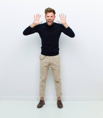 Panik ya da öfke içinde çığlık atan genç bir vücut adamı, şok olmuş, korkmuş ya da öfkeli, elleri başının yanında beyaz arka planda.