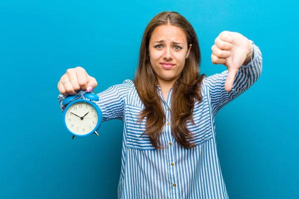 Mujer joven con despertador contra fondo azul — Foto de Stock