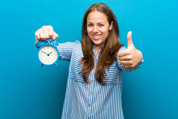 Mujer joven con despertador contra fondo azul — Foto de Stock