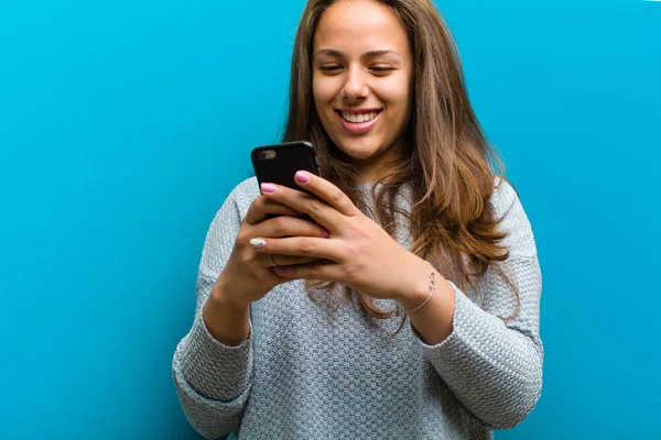 Ung kvinna med mobiltelefon mot blå bakgrund — Stockfoto