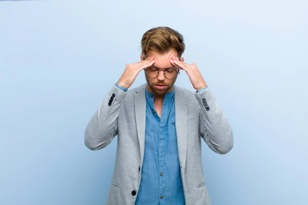 young businessman looking stressed and frustrated, working under pressure with a headache and troubled with problems against blue background