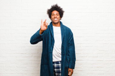 Genç siyah adam pijamalı, gülümseyen ve arkadaş canlısı görünen, iki ya da ikinci eli önde, tuğla duvara doğru geri sayıyor.