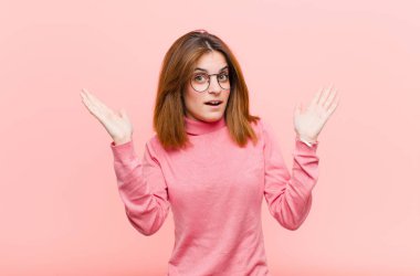 Genç, güzel bir kadın pembe arka plana karşı inanılmaz bir şey fark edince şaşırmış ve şaşırmış görünüyor.