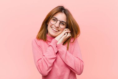 Genç, güzel bir kadın aşık ve sevimli görünüyor. Sevimli ve mutlu. Elleri pembe arka planda romantik bir şekilde gülümsüyor.