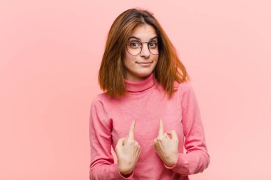 Genç ve güzel bir kadın, şaşkın ve şaşkın bir bakışla kendini işaret ediyor. Pembe arka plana karşı seçildiği için şaşırmış ve şaşırmış.