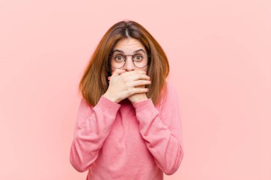 Genç ve güzel bir kadın elleri ile ağzını kapatıyor, şok olmuş, şaşırmış bir ifadeyle, bir sır saklıyor ya da pembe arka plana karşı 
