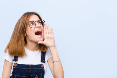 Genç ve güzel bir kadın öfkeyle bağırıyor. Yan taraftaki boşluğu kopyalamak için. Elleri ağzının yanında, mavi arka planda.