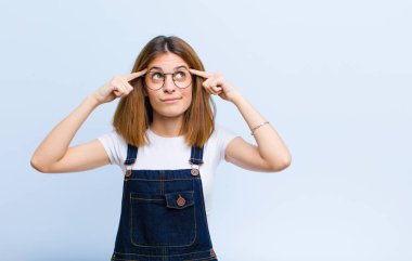 Genç ve güzel bir kadın konsantre olmuş ve bir fikir üzerinde kafa yoruyor, mavi arka plandaki bir soruna bir çözüm hayal ediyor.