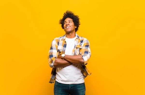 年轻的黑人男子感到快乐 充满希望 或思考 仰起头 交叉双臂靠着橙色墙壁复制空间 — 图库照片