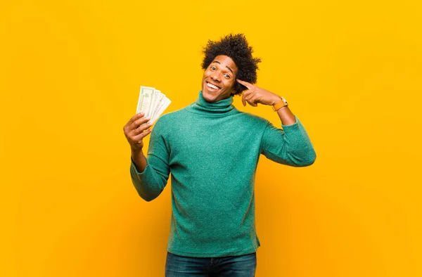 Joven afroamericano hombre con billetes de dólar contra naranja espalda —  Fotos de Stock