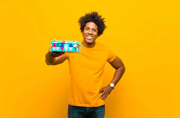 Молодой африканский американец с подарочной коробкой против оранжевого backgr — стоковое фото