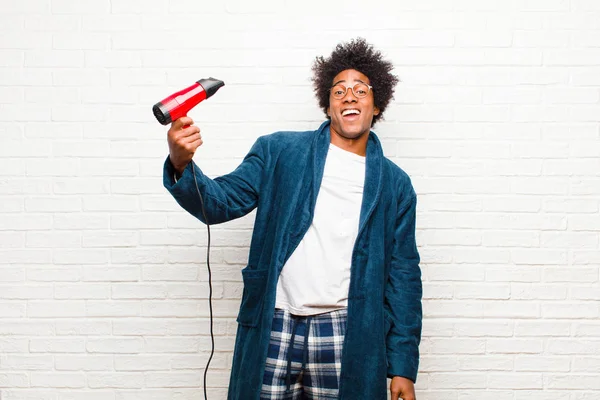 young black man wearing pajamas with a hair dryer against brick
