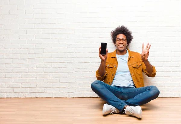 Jeune homme noir avec un téléphone intelligent assis sur le sol — Photo