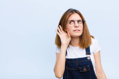 Genç ve güzel bir kadın ciddi ve meraklı görünüyor, dinliyor, gizli bir konuşma ya da dedikodu duymaya çalışıyor, mavi arka plana kulak misafiri oluyor.