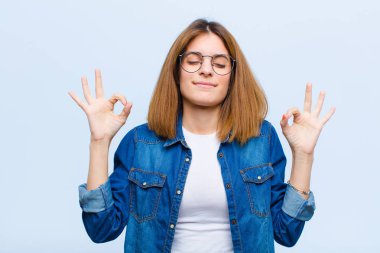 Genç ve güzel bir kadın konsantre olmuş ve meditasyon yapıyor, tatmin olmuş ve rahatlamış hissediyor, düşünüyor ya da mavi arka plana karşı bir seçim yapıyor.