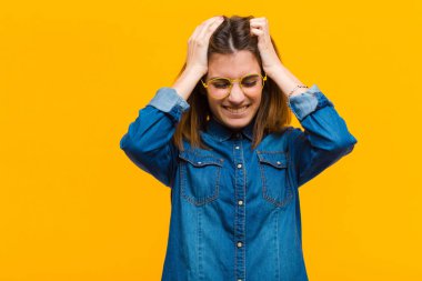 Genç ve güzel bir kadın stresli ve hayal kırıklığına uğramış hissediyor, el ele tutuşuyor, yorgun, mutsuz ve sarı arka planda migreni var.