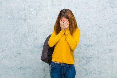Genç bayan öğrenci üzgün, hayal kırıklığına uğramış, gergin ve bunalımda, iki eliyle yüzünü kapatıyor, grunge duvarına karşı ağlıyor.