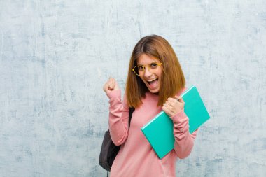 Son derece mutlu ve şaşırmış görünen genç bir bayan, başarıyı kutluyor, bağırıyor ve homurdanarak duvara zıplıyor.