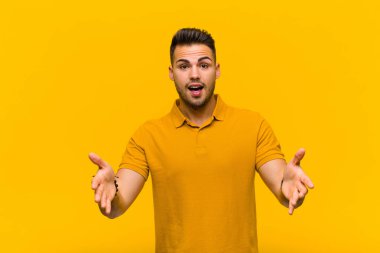 Genç İspanyol adam kendini mutlu, şaşkın, şanslı ve şaşırmış hissediyor. Sanki her şeyi ciddiye alıyor gibi. Turuncu duvara karşı inanılmaz.