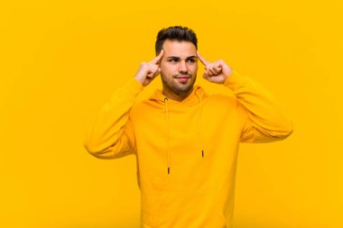 Latin kökenli genç adam bir fikre odaklanmış ve kafa yoruyor. Turuncu duvara karşı bir sorun ya da meydan okumaya çözüm düşünüyor.