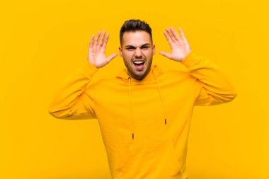 Panik ya da öfke içinde bağıran genç İspanyol adam, şok olmuş, korkmuş ya da öfkeli, elleri turuncu duvara dayalı.