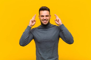 Genç İspanyol adam gergin ve umutlu, dua ediyor ve turuncu duvara karşı iyi şanslar diliyor.