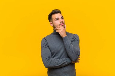 Genç İspanyol adam düşünceli, meraklı ya da hayal kuruyor, hayal kuruyor ve turuncu duvara karşı boşluğu kopyalamak için yukarı bakıyor.