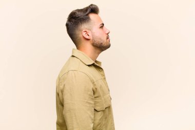 Profil görünümlü genç İspanyol adam uzayı kopyalamaya çalışıyor. İzole edilmiş arka plana bakarak düşünüyor, hayal ediyor ya da hayal kuruyor.